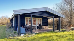 Eine Blockhütte mit überdachter Terrasse, Sitzgelegenheiten im Freien und einem Grill.