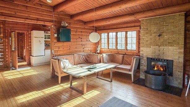 Ein rustikales Holzblockhaus-Interieur mit Holzboden, einer Couch, einem Tisch, einem Kamin und einem Fenster.