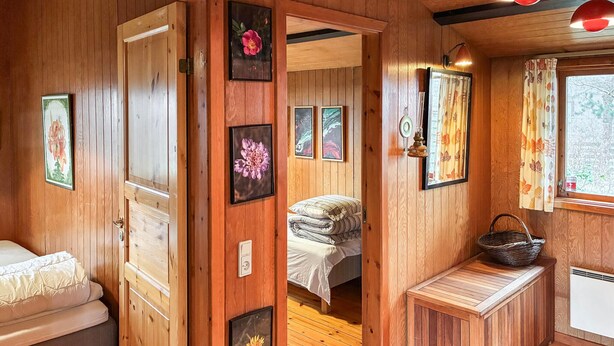 Interior de una cabaña de madera con una cama, un banco y cuadros en las paredes.