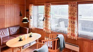Una habitación acogedora con detalles de madera, una mesa redonda de madera, un banco y dos ventanas con cortinas.