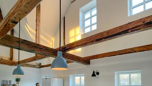 Een kamer met zichtbare houten balken, hanglampen, een koelkast en ramen.