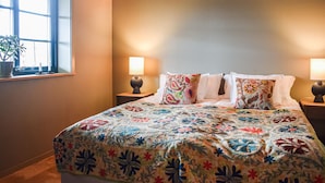 A bedroom with a bed, two bedside lamps, a window with a plant, and a wall with a light switch. - 1 bedroom cozy home in Kivik (Kivik)