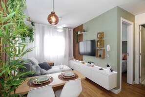Ein modernes Wohnzimmer mit Essbereich, einem an der Wand montierten Fernseher und einer Tür zu einem weiteren Raum.