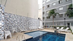Una piscina con paredes de azulejos, sillas de descanso blancas y una palmera.