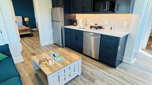 Eine moderne Küche mit dunklen Schränken, einem Edelstahl-Kühlschrank, einer Mikrowelle und einem Geschirrspüler. Ein Holztisch steht vor Zeitschriften und einer kleinen Pflanze.