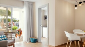 A modern living room with a sofa, a round table, and a dining area with chairs. There is a kitchen visible through an open door. - 1 Bedroom Junior Suite with kitchen, Pool and Garden Views, Full Bathroom, 40sq Metres, Balcony, Lar (Corralejo)