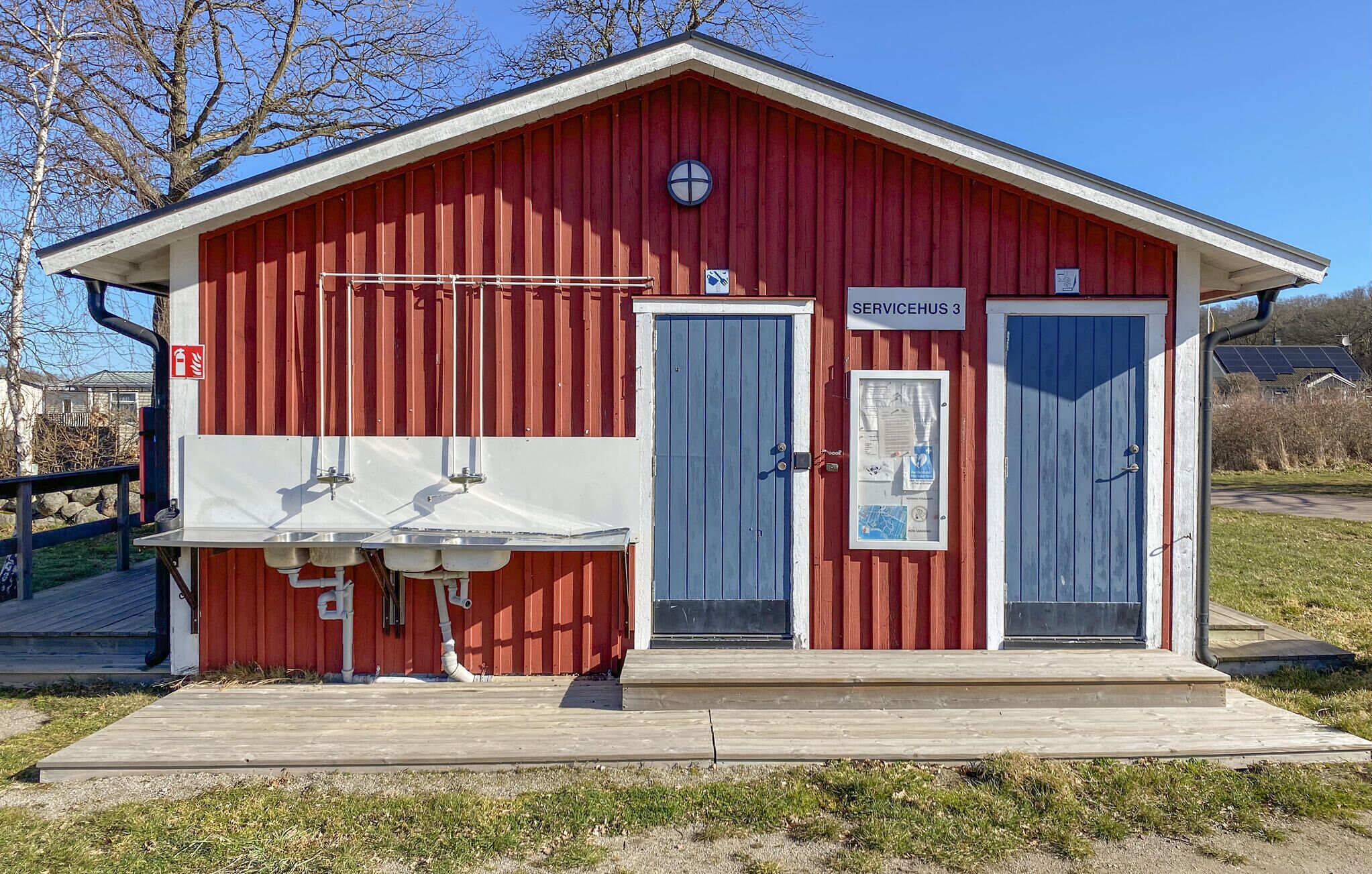 Een rood gebouw met twee deuren, een klein portaal en een bord met de tekst 'SERVICEHUS 3'.
