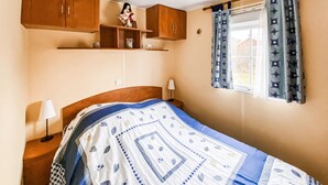 Une chambre à coucher avec un lit, des armoires en bois, une fenêtre avec des rideaux et une table de chevet avec une lampe.