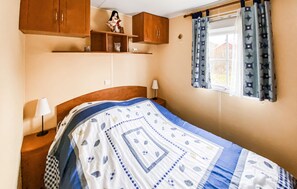 A bedroom with a bed, wooden cabinets, a window with curtains, and a nightstand with a lamp. - 3 bedroom pet friendly home in Färjestaden (Färjestaden)