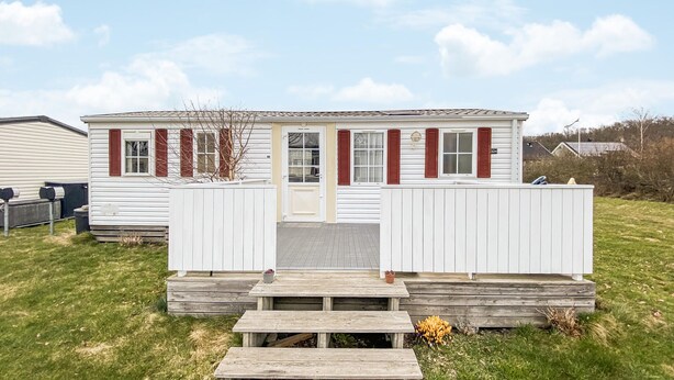 Une maison mobile de plain-pied, avec un porche à l’avant, une boîte aux lettres et le numéro « 324 » sur le côté.