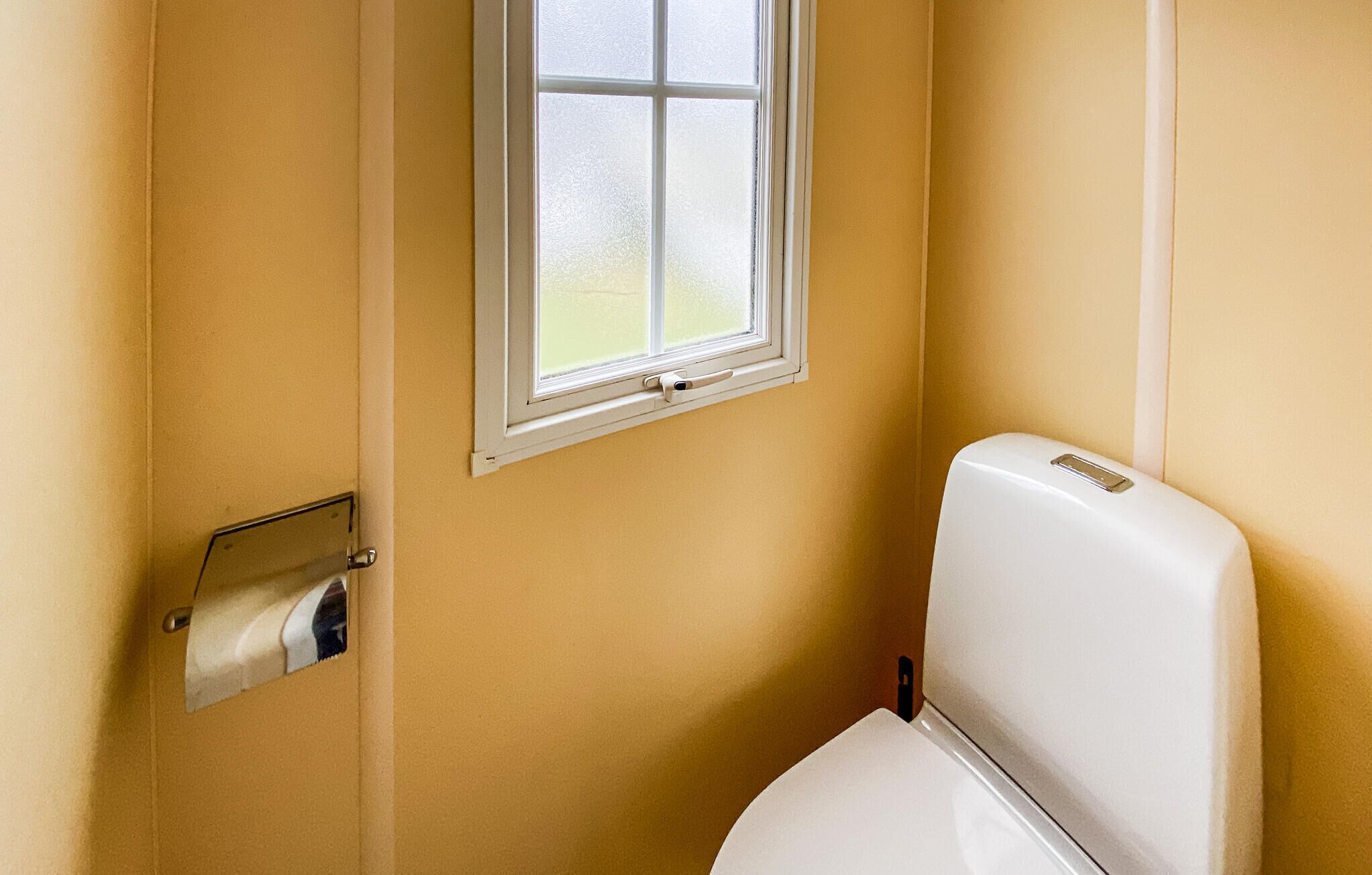 A bathroom with a toilet, a window, and a paper towel dispenser.