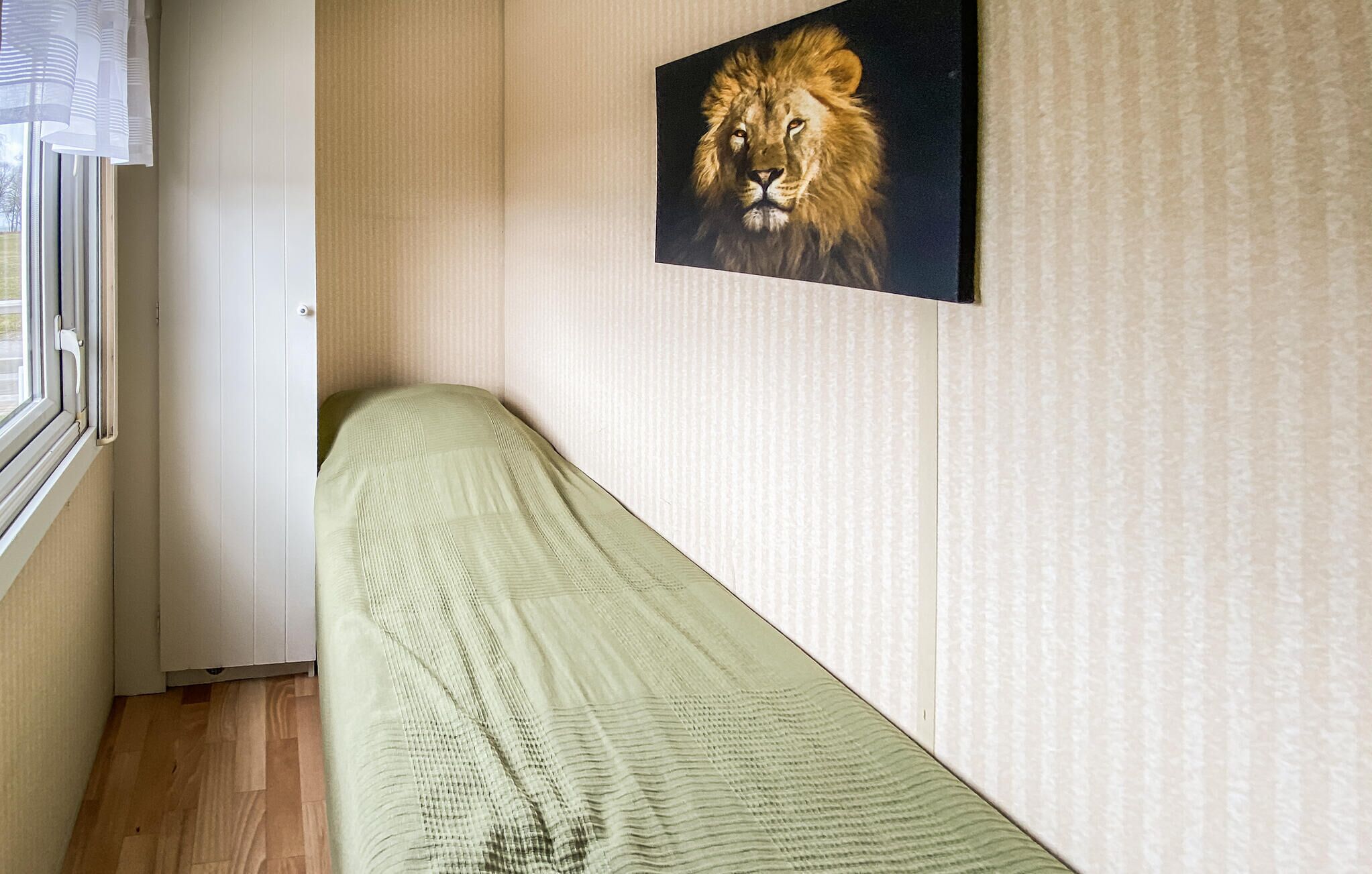 En säng för en person i ett rum med ett fönster, en tavla med ett lejon på väggen och en vägg med en intressant yta.