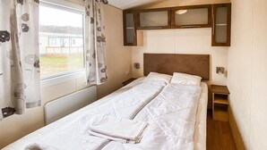 Un lit simple avec une couette, une fenêtre avec des rideaux, une tête de lit et une petite table de chevet.