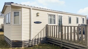 Une maison mobile avec une enseigne indiquant « Séville », une terrasse en bois et un espace clôturé.