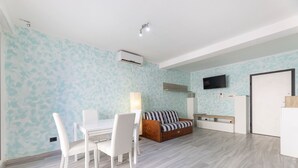 Ein modernes Wohnzimmer mit Essbereich, einer Couch, einem an der Wand montierten Fernseher und einer Klimaanlage.