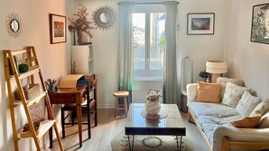 Un soggiorno accogliente con un divano, un tavolino, una sedia di legno, uno sgabello, una libreria e una finestra con tende.