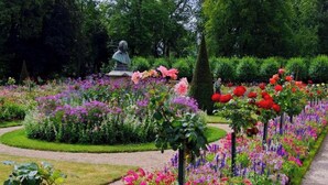 Un giardino con una statua, fiori diversi e un prato curato.