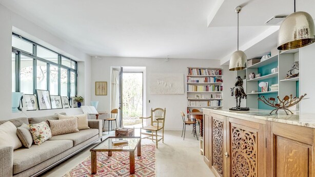 Ein geräumiges Wohnzimmer mit einer Couch, einem Couchtisch und Sesseln, eine Küche mit Holzausbau und ein Bücherregal voller Bücher.