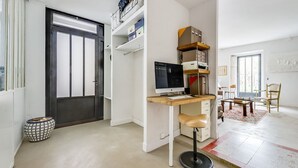 Ein Zimmer mit Schreibtisch, Computer, Stuhl und einer Tür zu einem weiteren Raum.