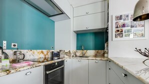 Eine kompakte Küche mit weißen Schränken, einer türkisblauen Spritzschutzwand, einem eingebauten Ofen und einem Spülbecken mit modernem Wasserhahn.