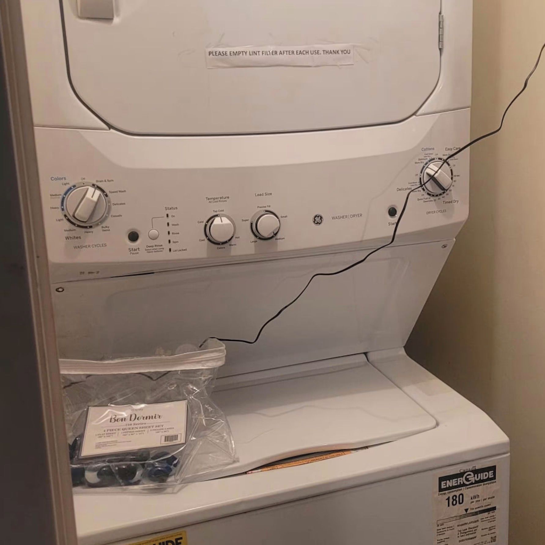 A front view of a washing machine with control knobs, a lint filter, and a Ben Dempsey detergent package.