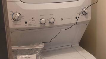 A front view of a washing machine with control knobs, a lint filter, and a Ben Dempsey detergent package.