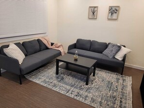 Een woonkamer met twee donkere banken, een salontafel en een vloerkleed met dessin.