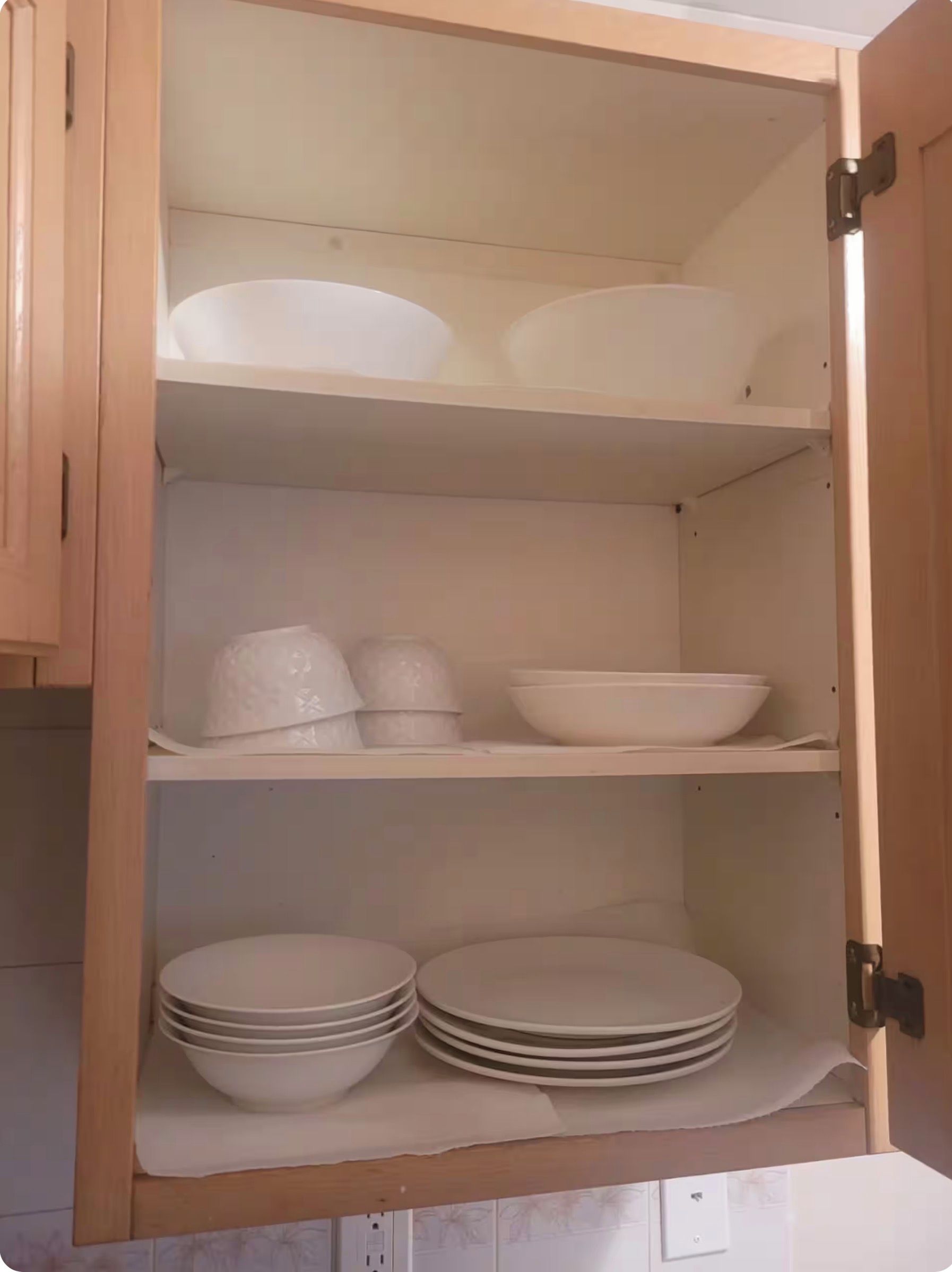 A wooden cabinet with shelves containing white bowls and plates.