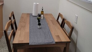 Un comedor con una mesa de madera, cuatro sillas, un cuadro en la pared, una ventana con persianas y una pequeña planta en maceta sobre la mesa.