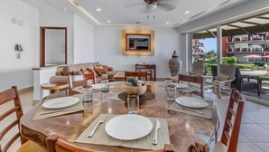 Un comedor con una mesa redonda preparada para cuatro personas, un sofá y un televisor montado en la pared.