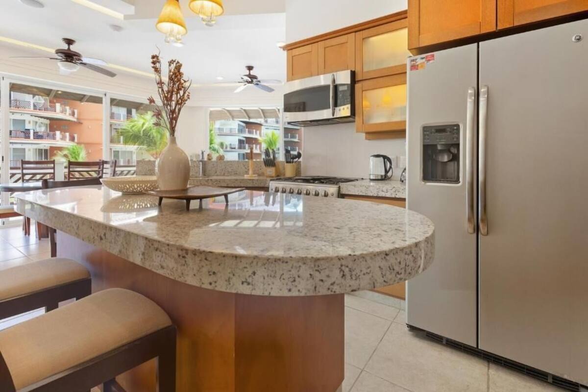A kitchen with granite countertops, stainless steel appliances, wooden cabinets, and a central island with seating.