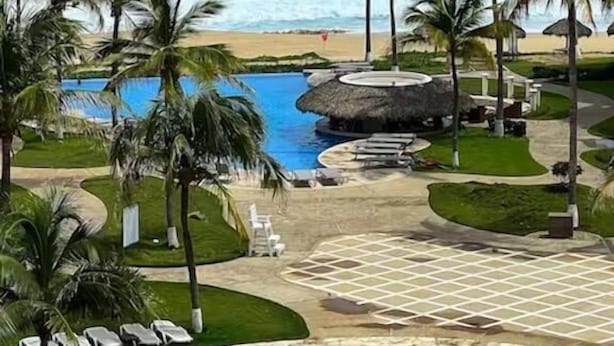 Un resort con piscina, palmeras y vista a la playa.