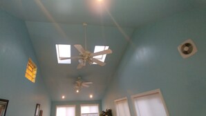 Une pièce dotée de deux ventilateurs de plafond, d’une fenêtre avec des stores et d’une bouche d’aération fixée au mur.