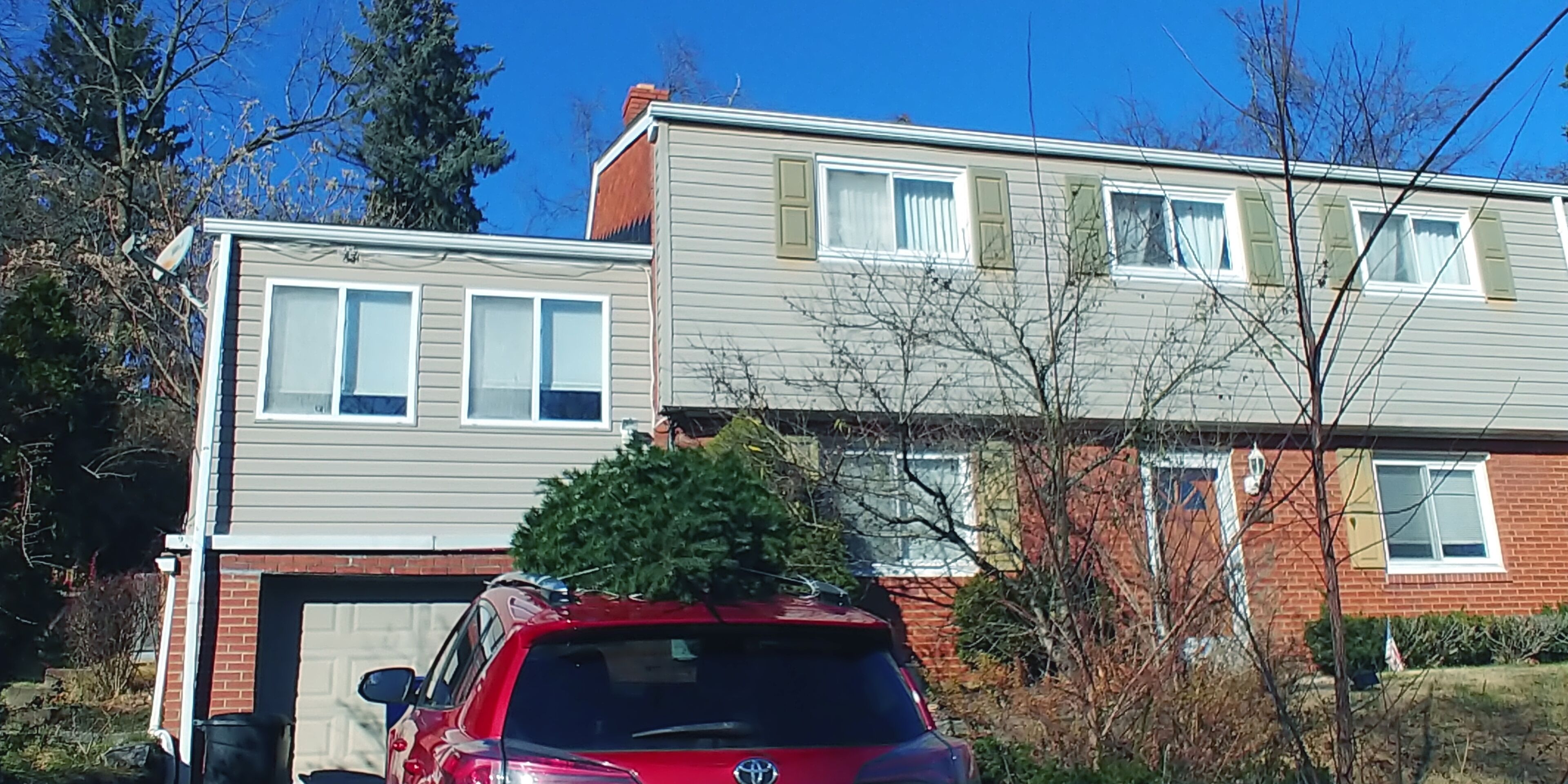 A two-story residential building with a garage, a red car parked in front, and a Christmas tree on the roof.