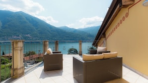 Una terrazza con mobili in vimini, vista su un lago e montagne sullo sfondo.