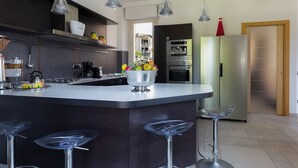 Una cucina moderna con isola centrale, sgabelli da bar, elettrodomestici in acciaio inossidabile e illuminazione a sospensione.