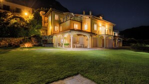 Una grande casa a più piani con un prato curato, un'area salotto esterna e un balcone.