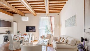 Una sala de estar con sofá, sillas, televisor, una zona de cocina y una mesa de comedor con manteles florales.