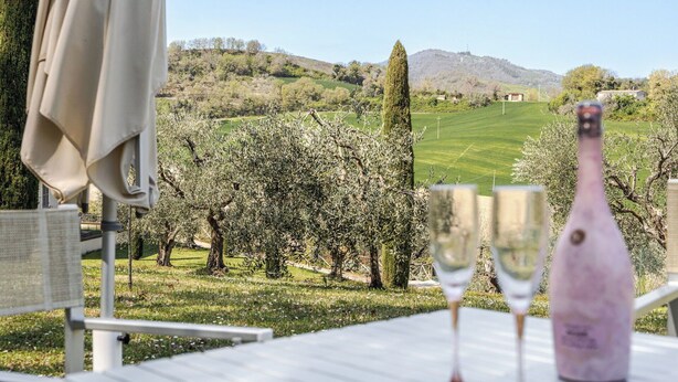 Mesa al aire libre con dos copas de vino y una botella, con vistas a un viñedo y una clara panorámica de las colinas.