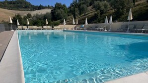 Una piscina rectangular con agua azul cristalina, rodeada de sillas de descanso y sombrillas.