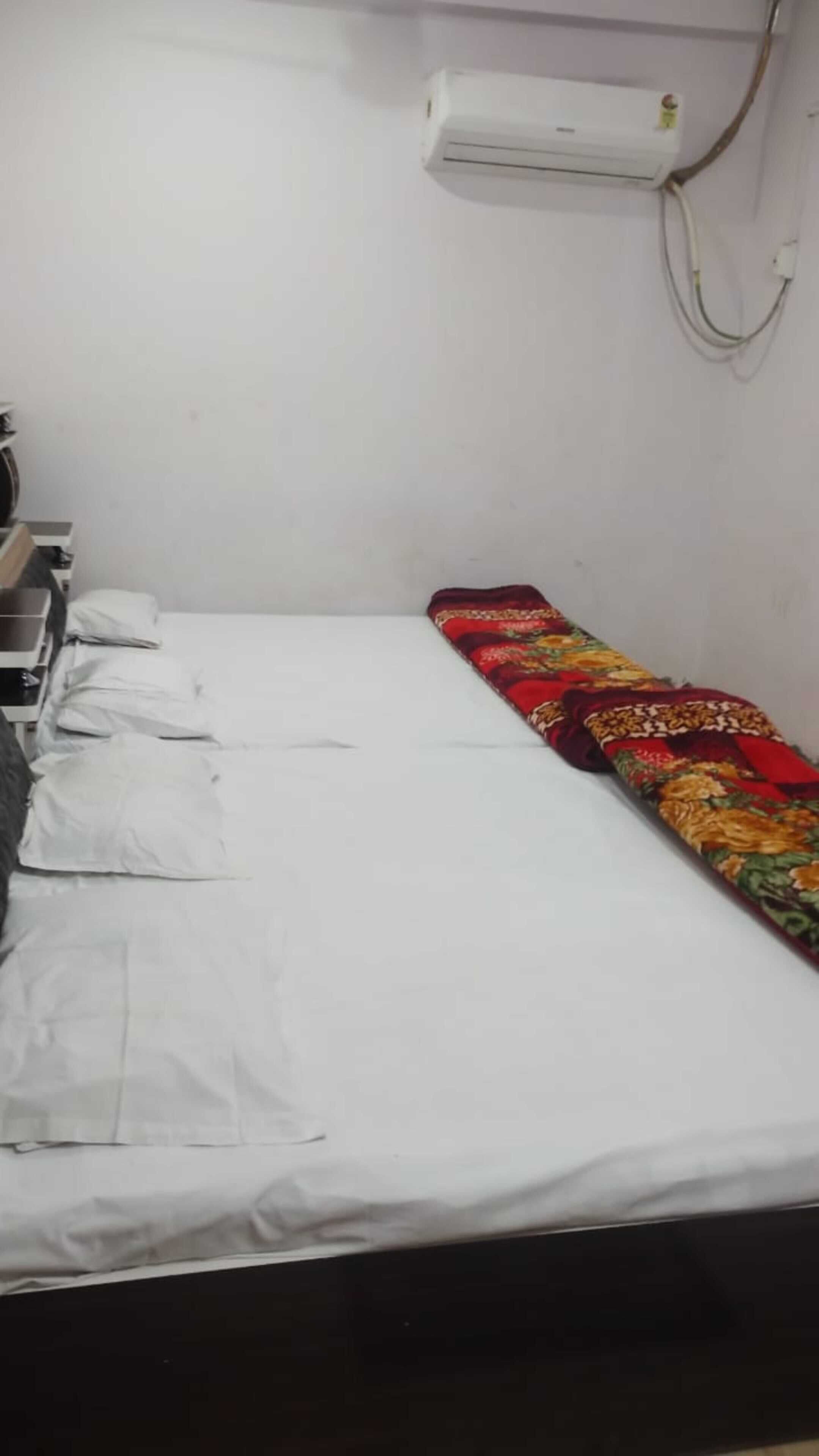 Una cama individual con sábanas blancas, una manta colorida y un aire acondicionado montado en la pared.