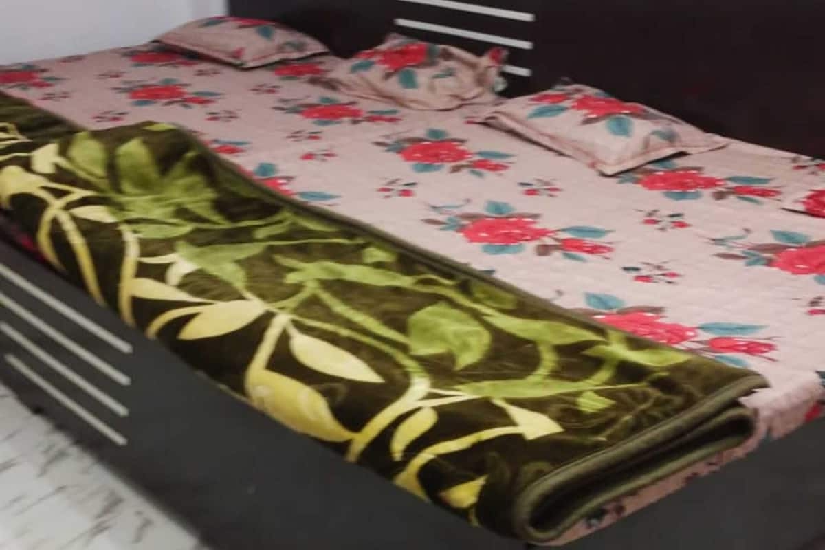 A bed with a floral bedspread, a black headboard, and a patterned floor.