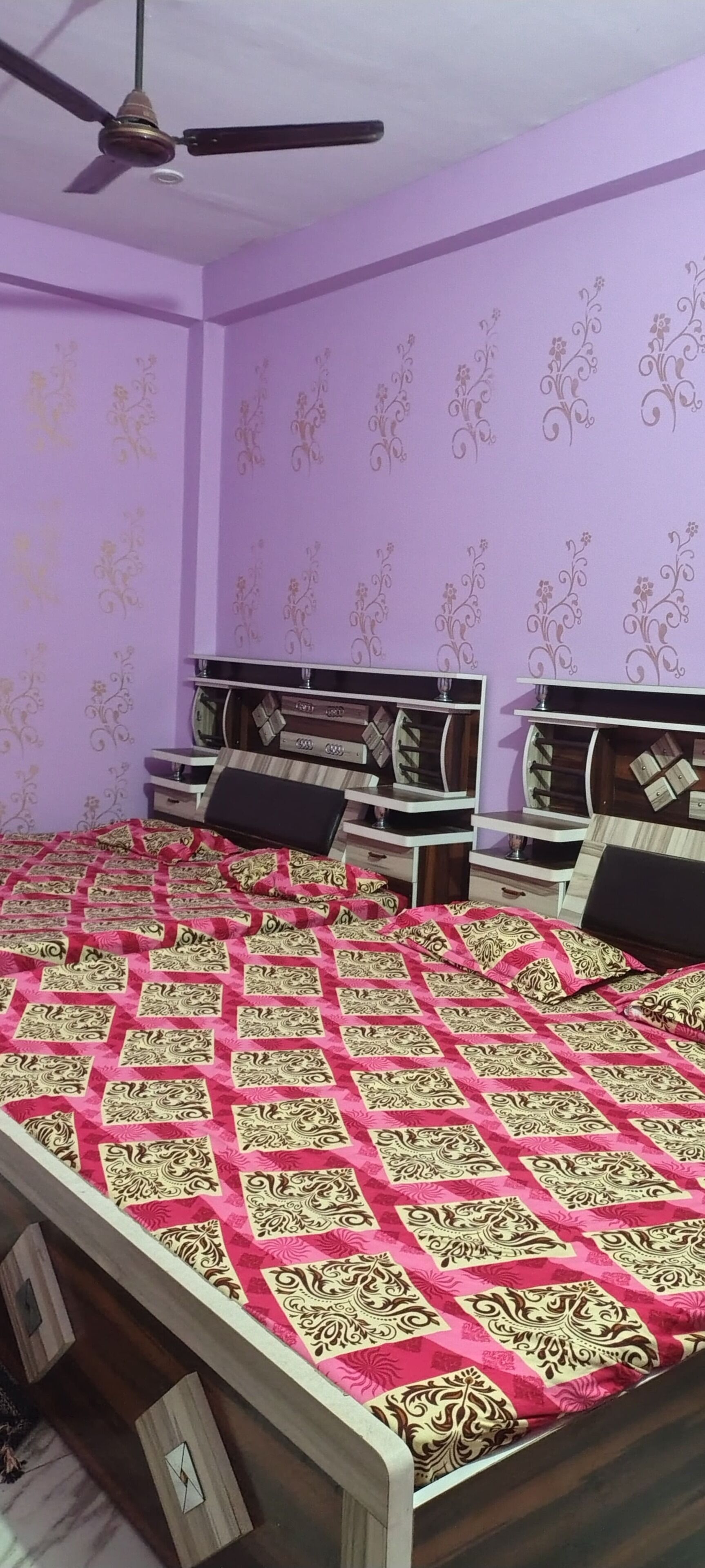 Un dormitorio con cama, dos mesitas de noche, ventilador de techo y papel tapiz estampado.