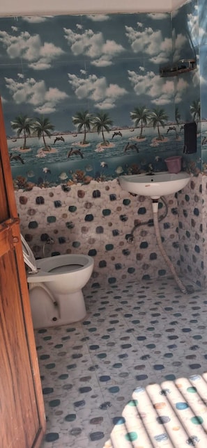 A bathroom with a toilet, sink, and shower. The walls have a tropical mural with palm trees and water.