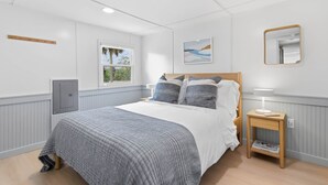 A bedroom with a bed, a bedside table with a lamp, a window, a wall-mounted mirror, and a door. - Seabreeze Cottage - Home in Steinhatchee Florida (Steinhatchee)