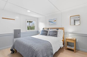 A bedroom with a bed, a bedside table with a lamp, a window, a wall-mounted mirror, and a door. - Seabreeze Cottage - Home in Steinhatchee Florida (Steinhatchee)