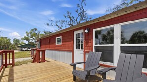 A red building with a wooden deck, two Adirondack chairs, and a white door. - Seabreeze Cottage - Home in Steinhatchee Florida (Steinhatchee)