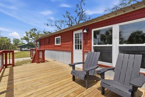 A red building with a wooden deck, two Adirondack chairs, and a white door. - Seabreeze Cottage - Home in Steinhatchee Florida (Steinhatchee)
