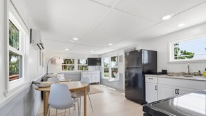 A modern kitchen with white cabinetry, a black refrigerator, and a dining area with a table and chairs. - Seabreeze Cottage - Home in Steinhatchee Florida (Steinhatchee)
