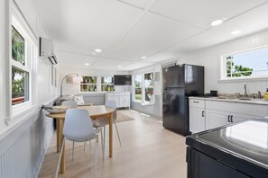 A modern kitchen with white cabinetry, a black refrigerator, and a dining area with a table and chairs. - Seabreeze Cottage - Home in Steinhatchee Florida (Steinhatchee)